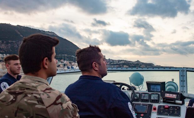 A Royal Navy sailor stands at the helm of a patrol boat