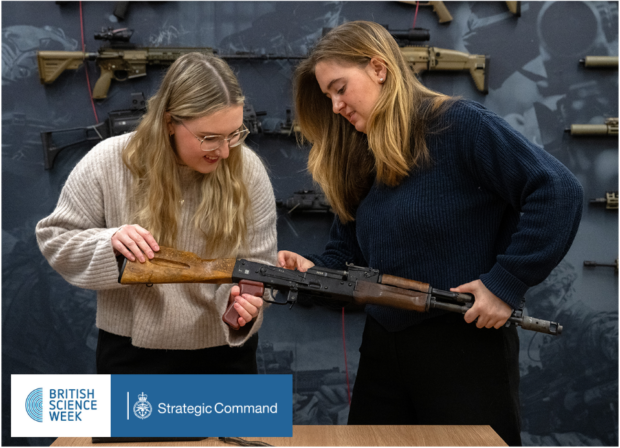 The image shows two women examining a rifle with a wooden stock. They are in a display room with various firearms mounted on the wall behind them. At the bottom of the image, there's a banner with logos for "British Science Week" and "Strategic Command".